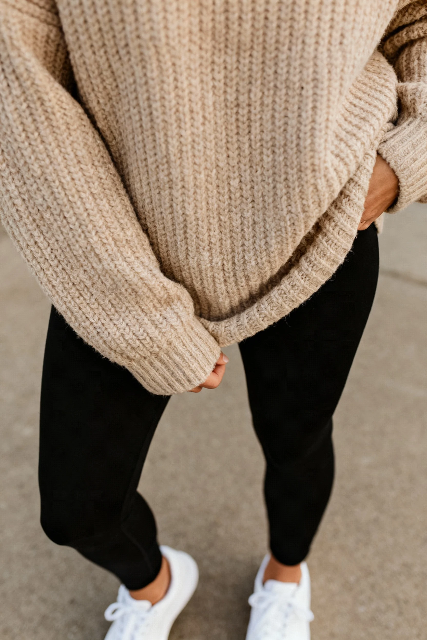 closeup female beige knit sweater half-tuck, black leggings, white sneakers