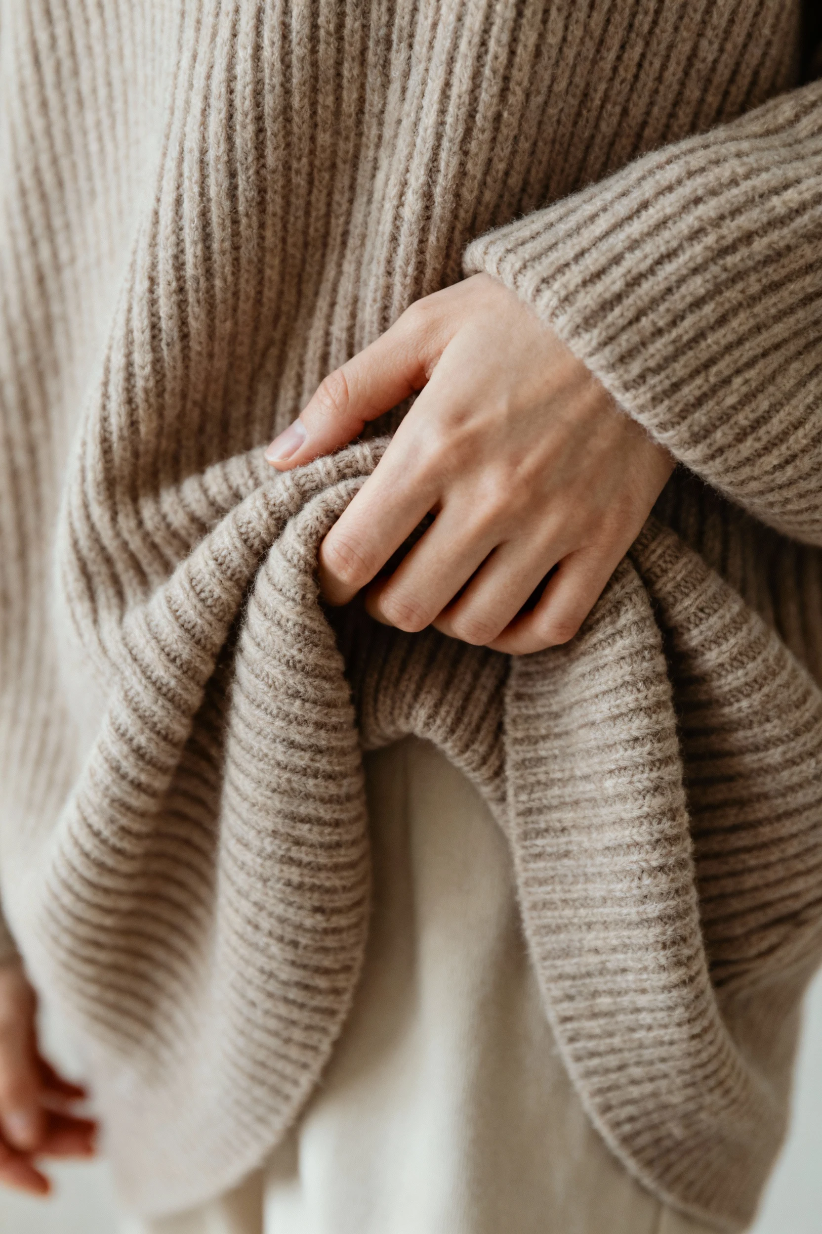 closeup of female hands French-tucking oversized ribbed knit sweater