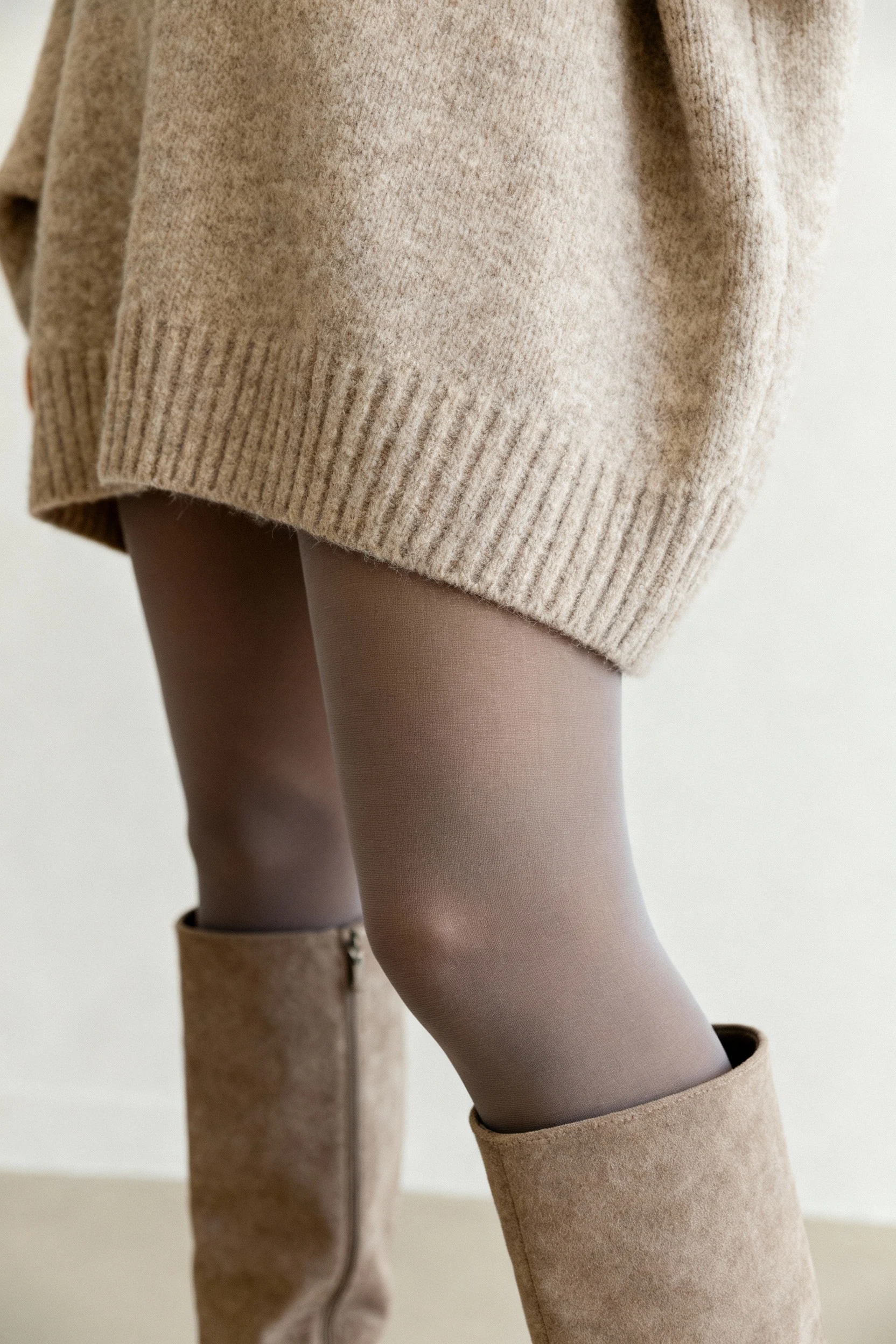 closeup of ribbed oversized sweater hem, opaque tights, knee-high boots