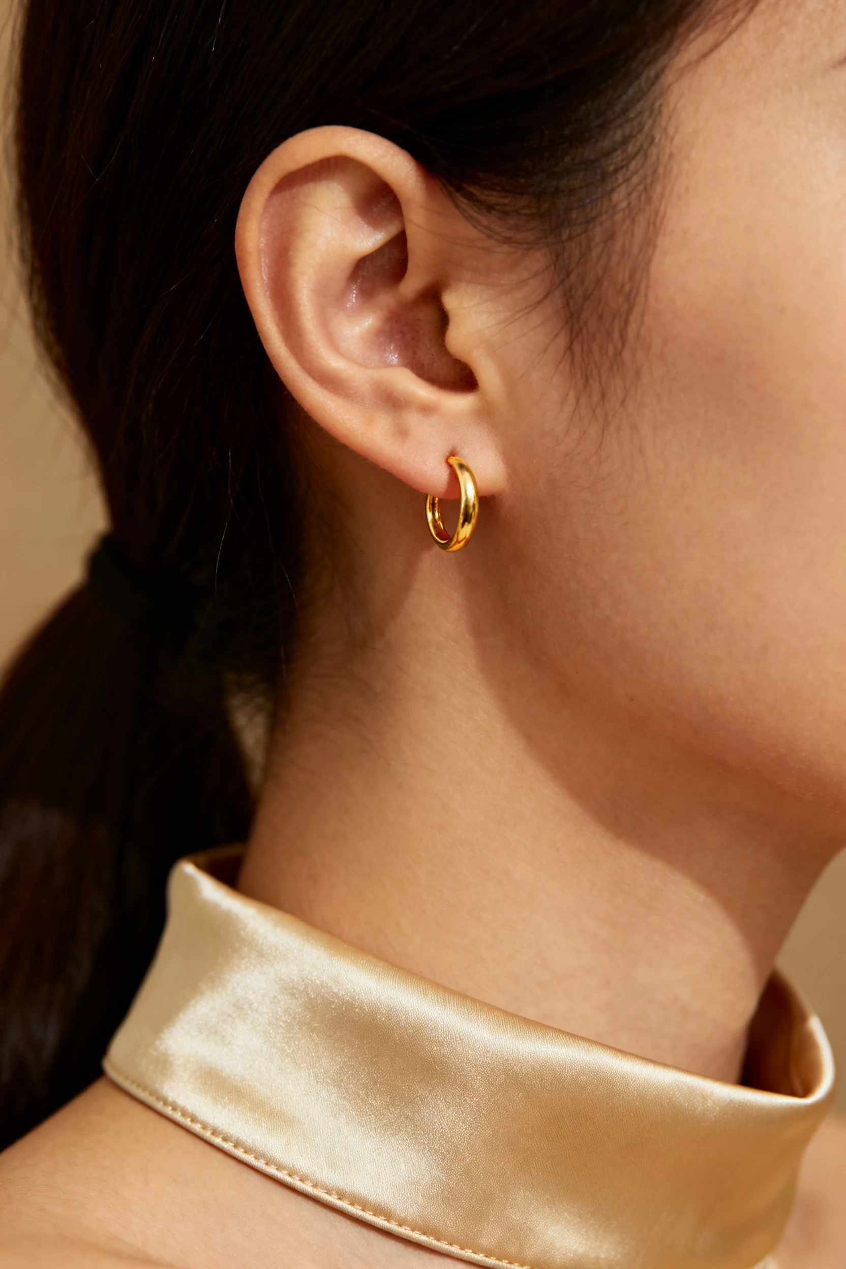 Closeup female ear, tiny gold hoop, champagne satin collar
