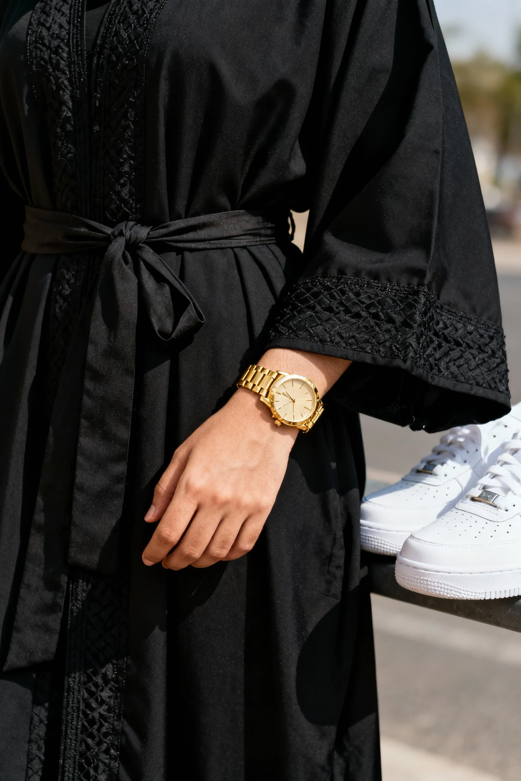 closeup of belted black abaya, gold watch, white sneakers
