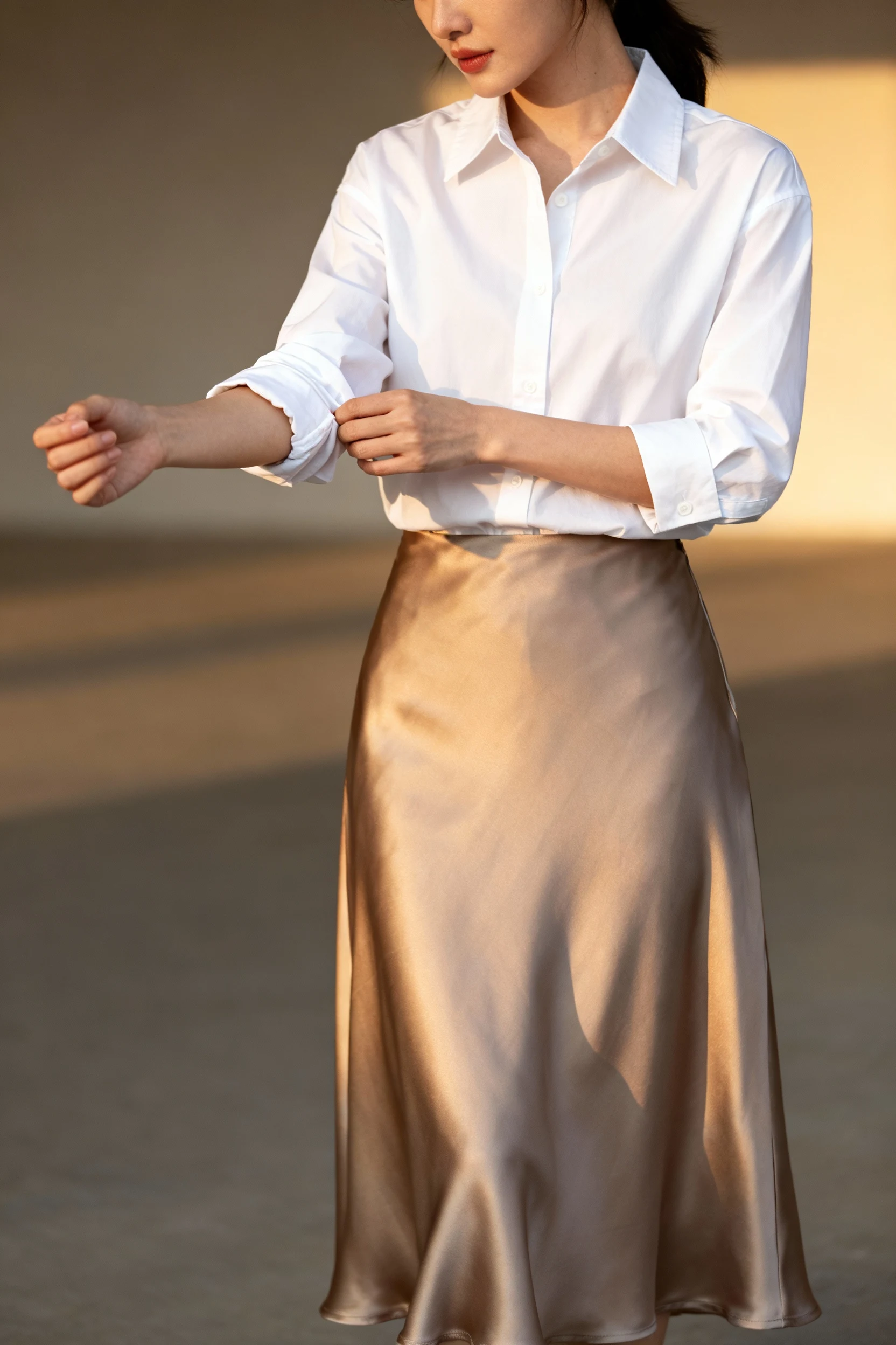 female rolling crisp white button-down sleeves over satin skirt
