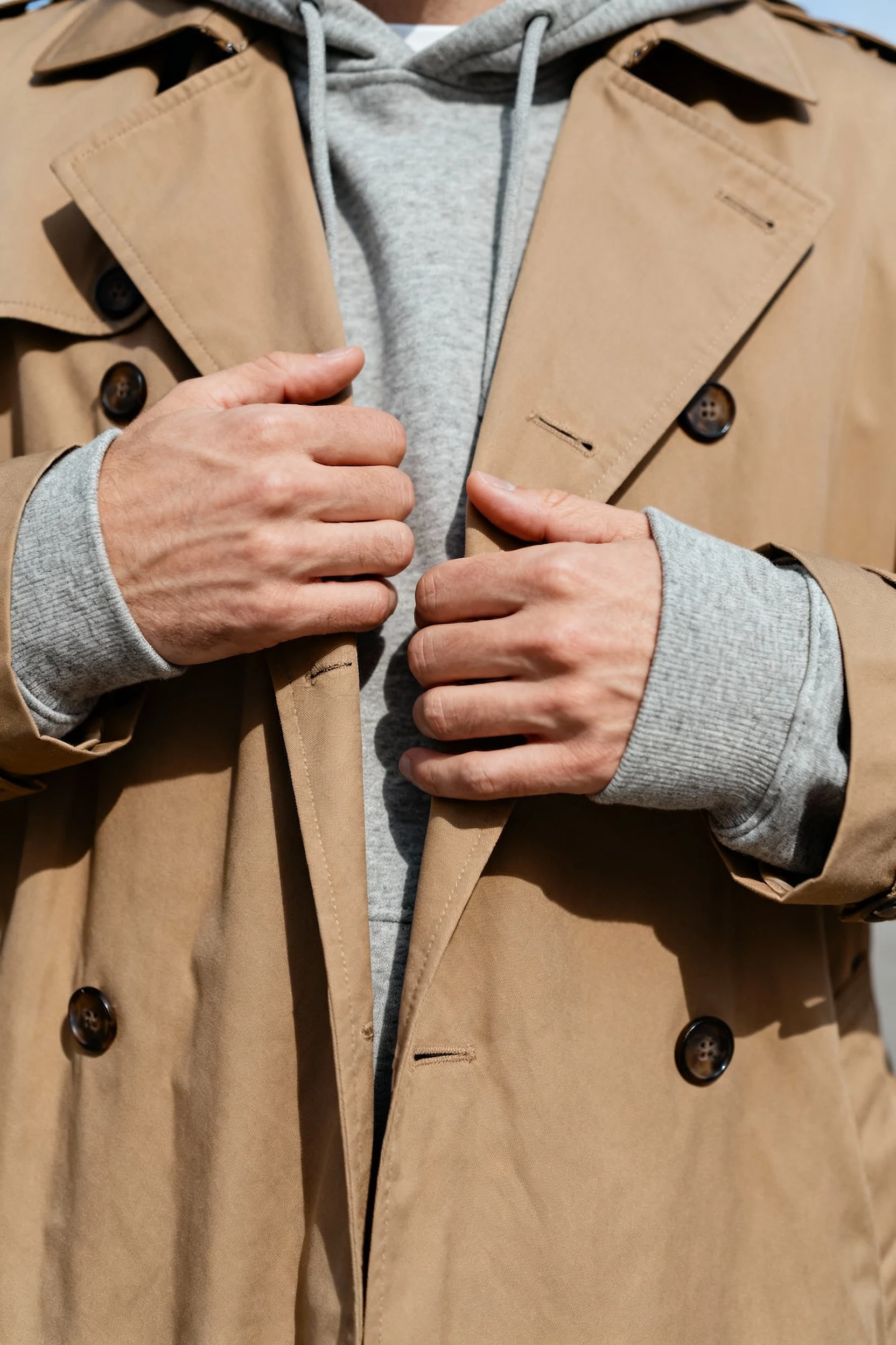 closeup male hands pushing gray hoodie sleeves through camel trench