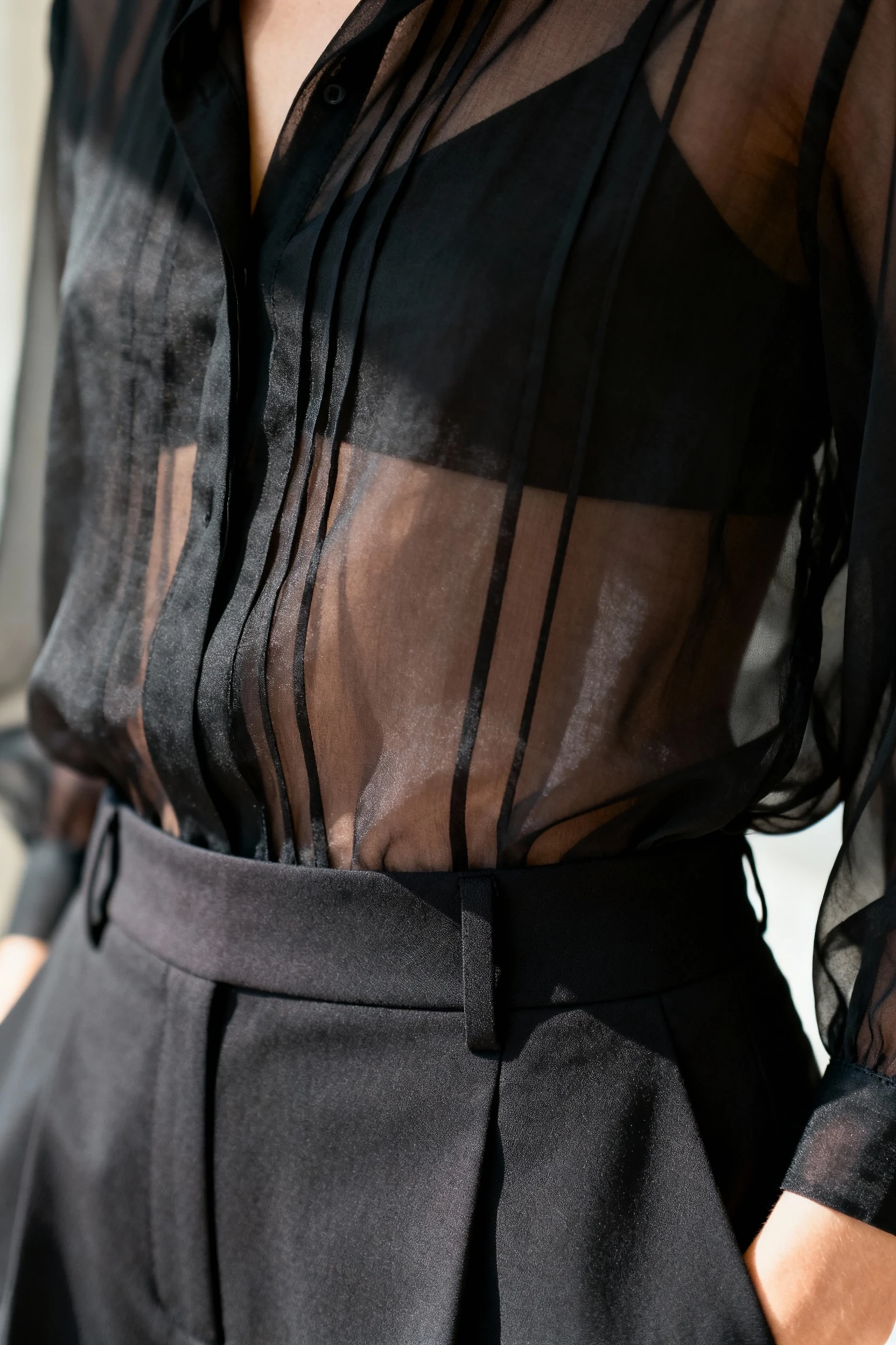 closeup of sheer black blouse fabric layered over high-waisted trousers