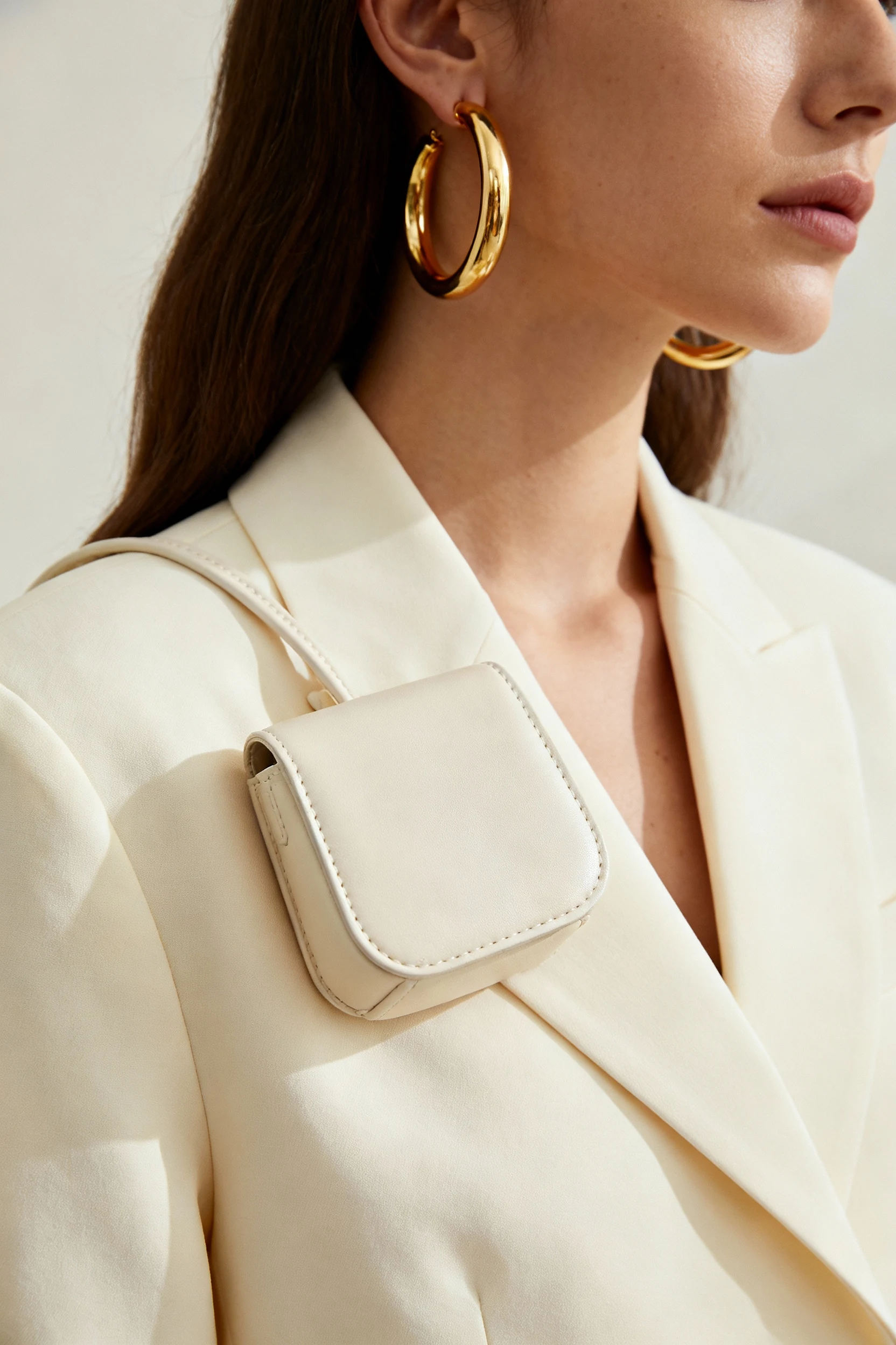 closeup female gold hoops, cream mini bag, cream blazer