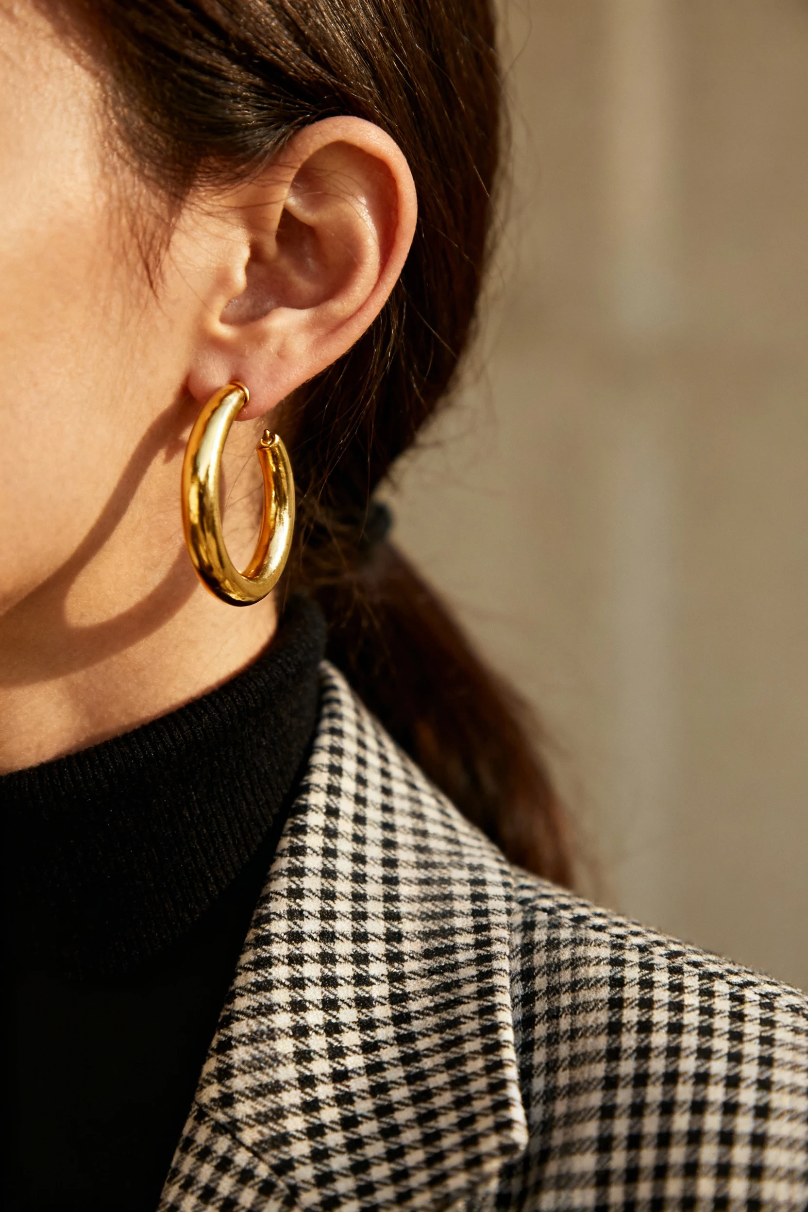 closeup female ear with gold hoops, plaid blazer, turtleneck