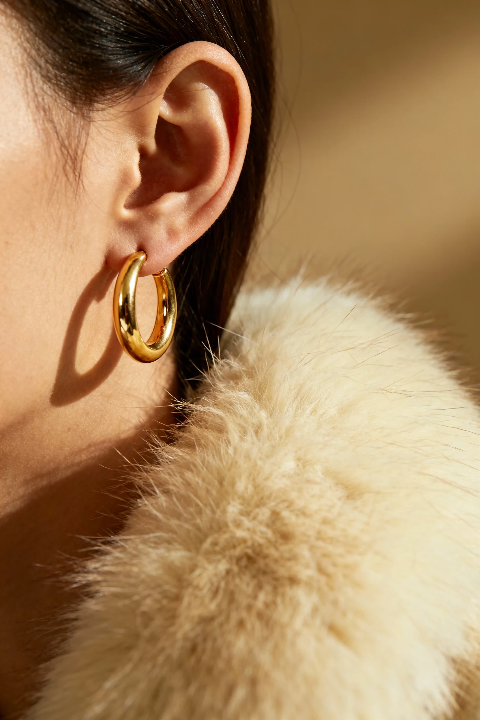 closeup female ear with gold hoop, faux fur coat collar