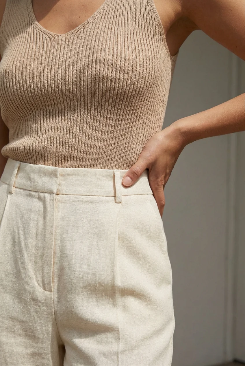 closeup female waist, ribbed beige tank, cream trousers