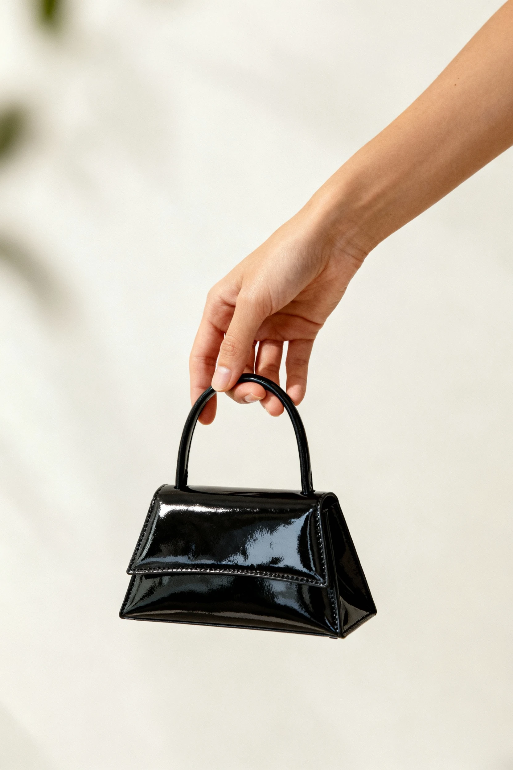female hand holding small black patent mini bag with structured shape