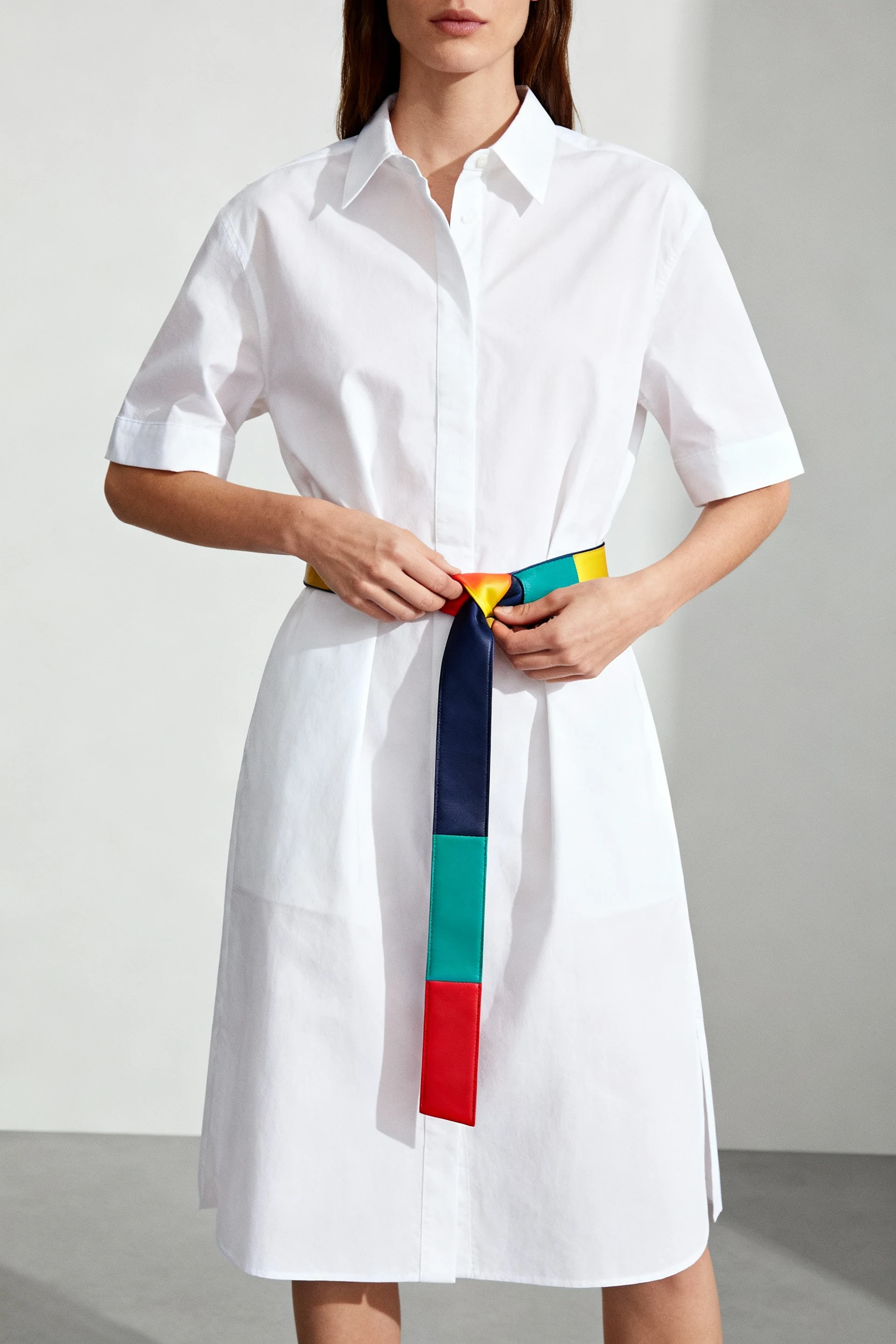 female tying wide colorful belt around crisp white cotton shirt dress