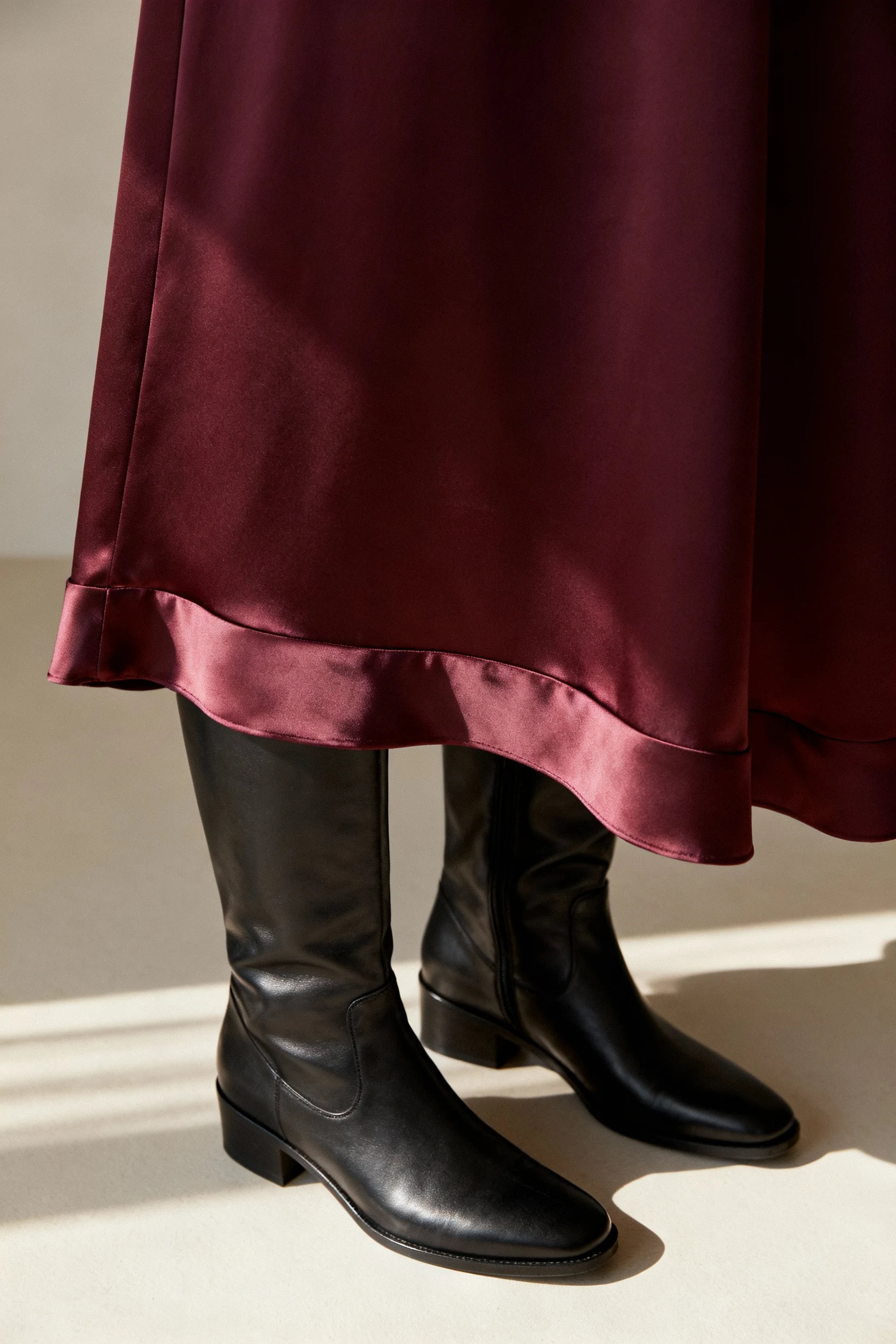 closeup knee-high boots beside satiny midi skirt hem