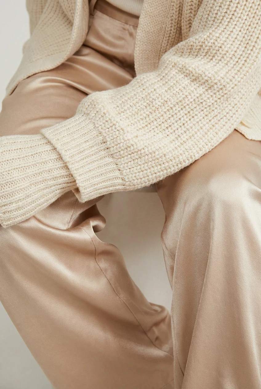 closeup of ribbed knit cardigan sleeve resting on flowy satin wide-leg pants