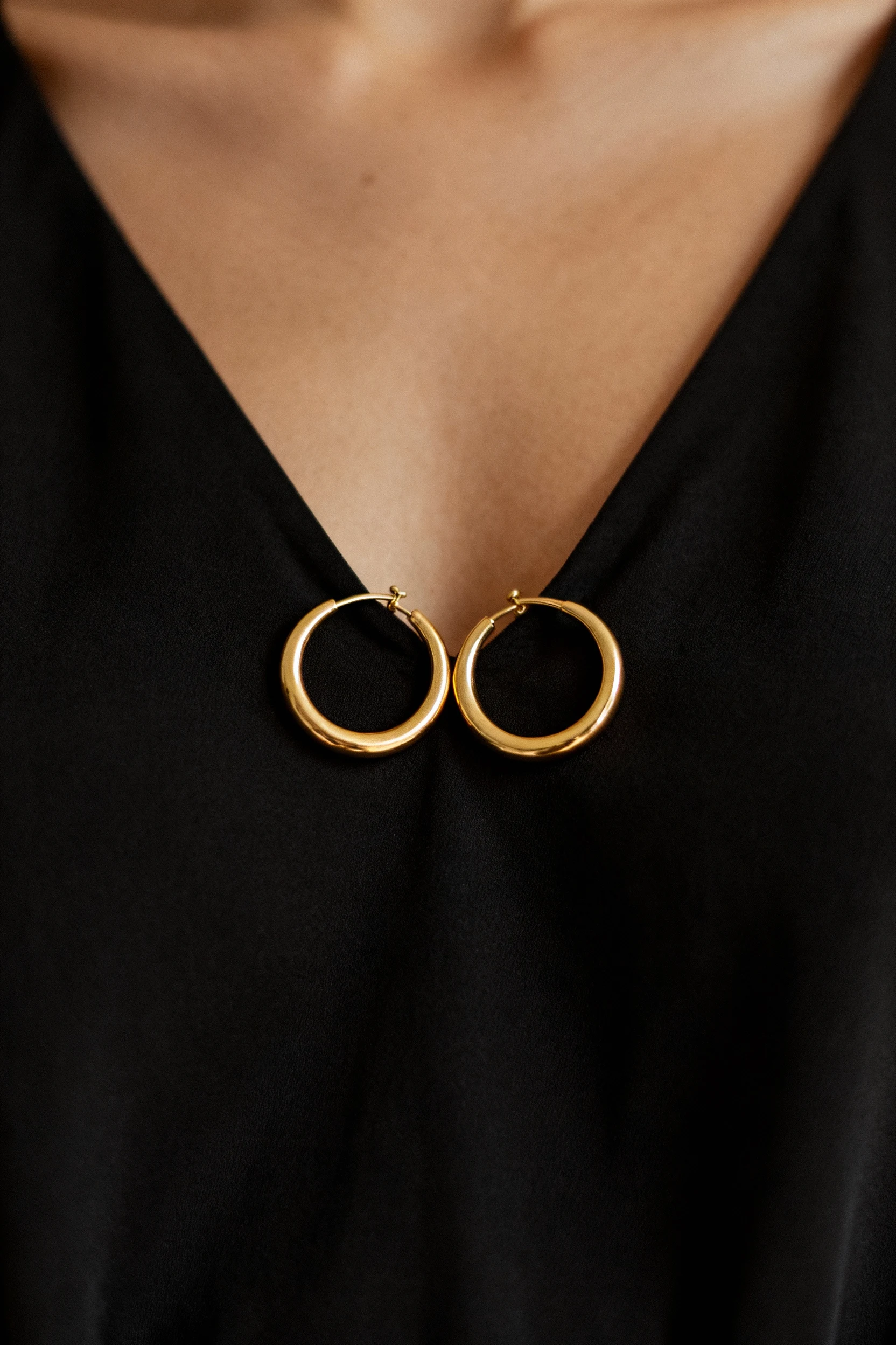 closeup of minimalist gold hoop earrings against black maxi dress neckline